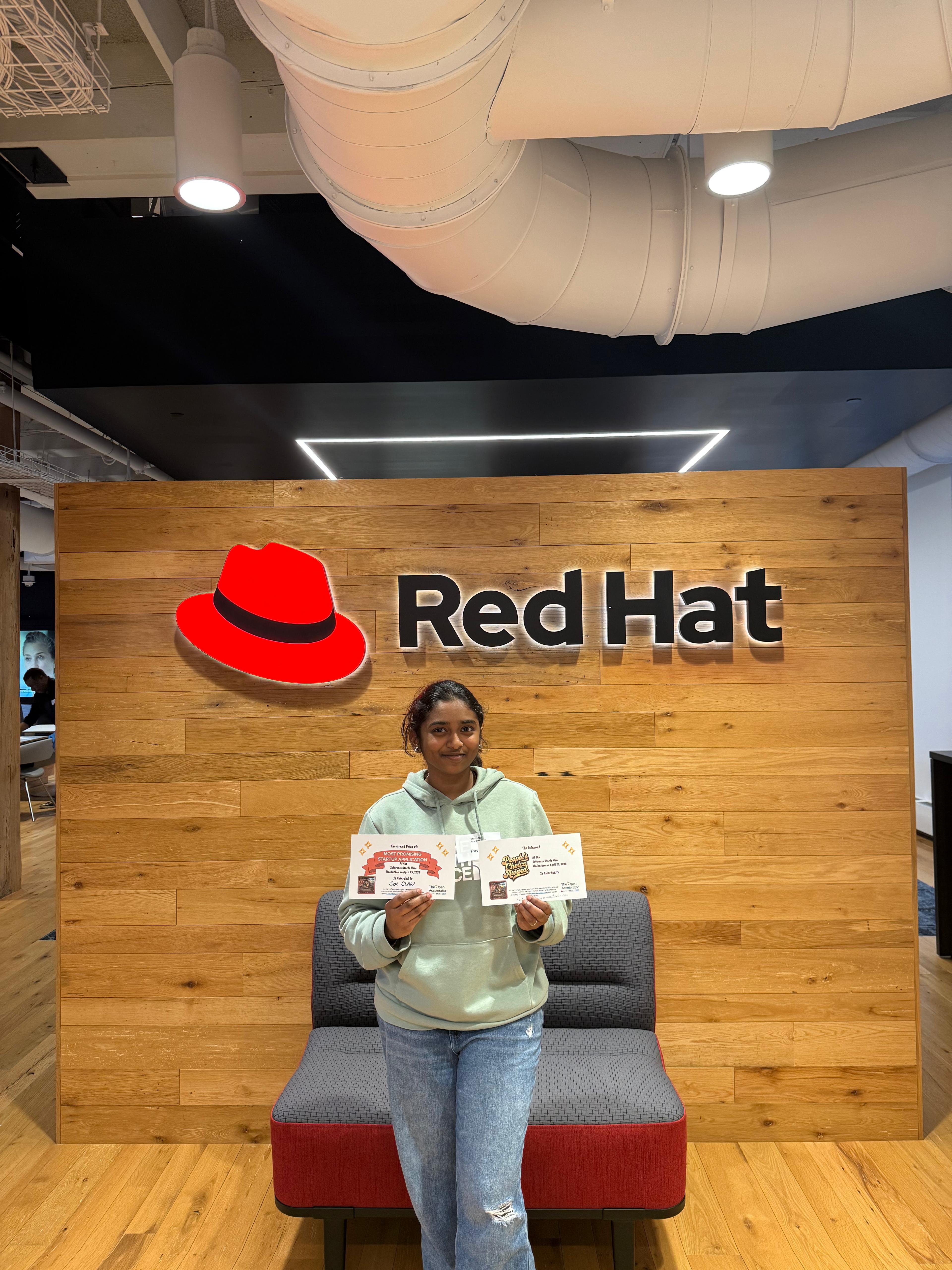 Pavithra holding two award certificates at Red Hat headquarters after winning Most Promising Startup App and People's Choice at the Open Accelerator Hackathon
